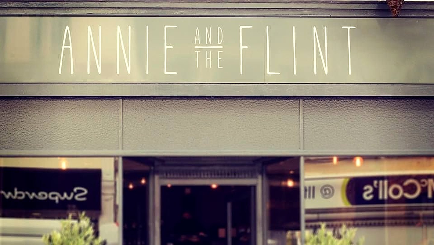 The Annie and the Flint shopfront: thin cream capitals on a grey fascia above a glass front, with small olive trees either side of the door